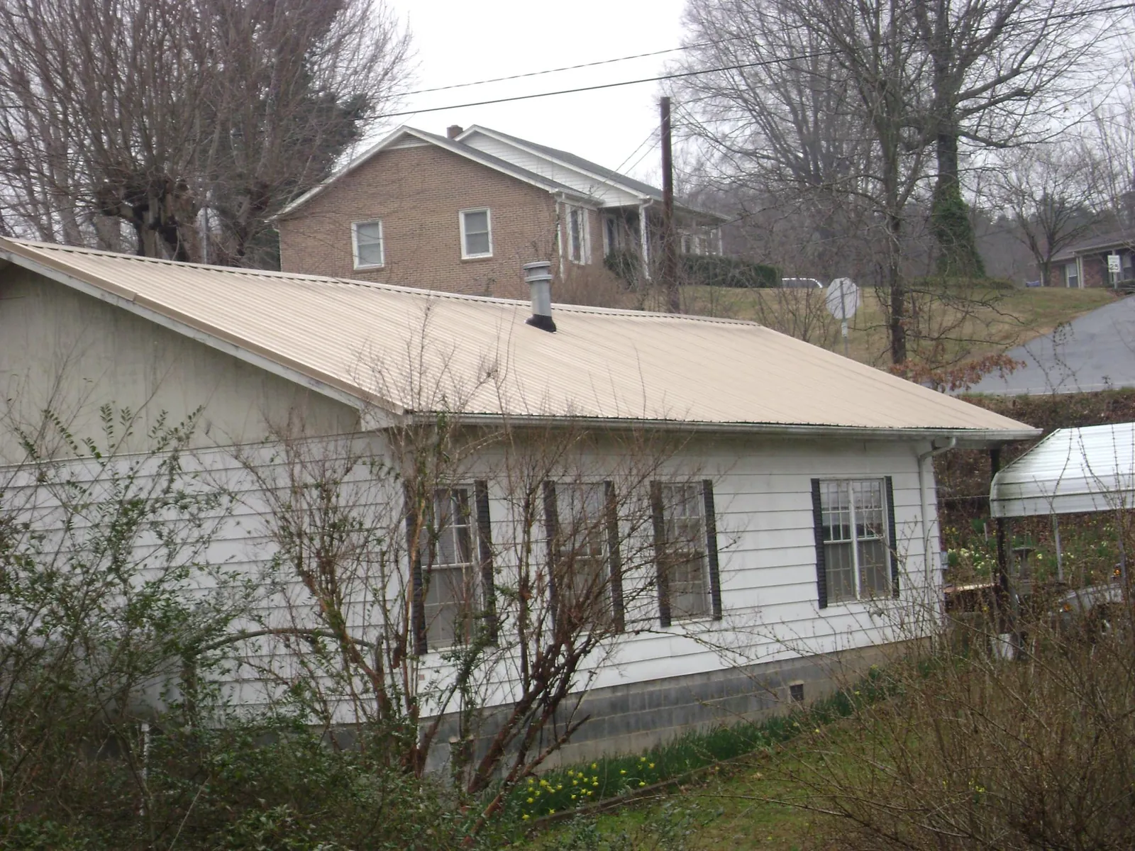 Tan metal roof on a white sided house set into a hillside — Commercial Roofing by Roofing Brothers in Fairview